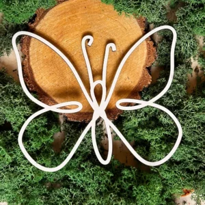 Scrapka motyl liniowy z białej tektury 1,5 mm, ułożona na tle plastra drewna i zielonego mchu.