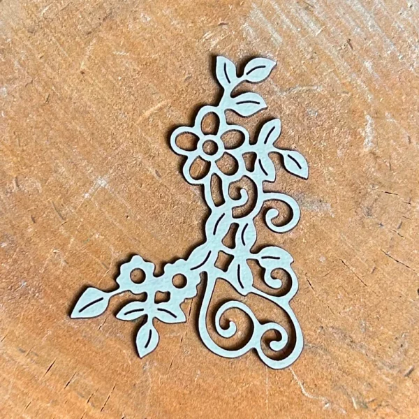 Kwiatowy ornament narożny wycięty z białej tektury 1,5 mm na drewnianym tle